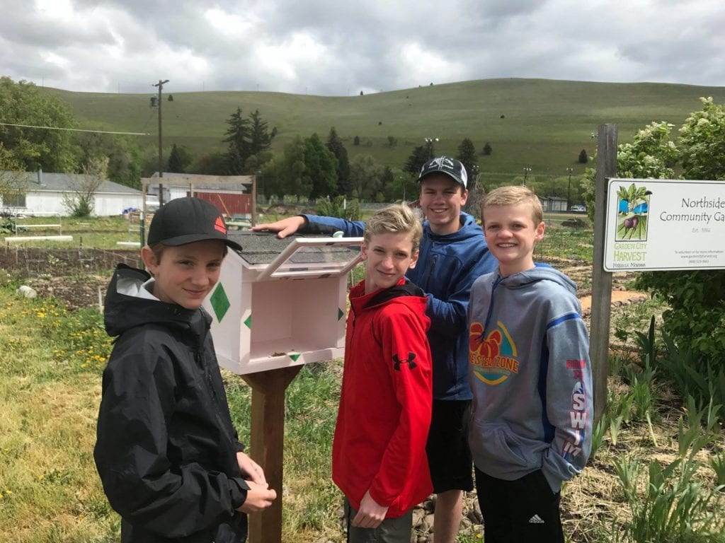 Four Boy Scouts smile after placing a new handcrafted little free library box in front of a community garden as volunteer work.